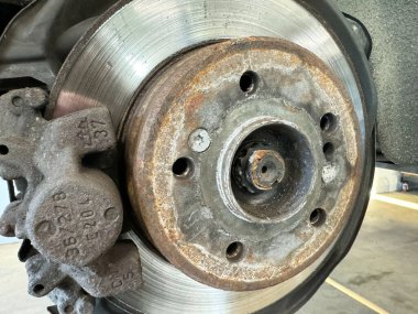 Close-up view of a rusty car brake disc and caliper in a garage setting clipart