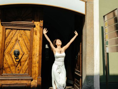 Güneş ışığında neşeli bir kadın tarihi ahşap kapının dışında kutlama yapıyor.