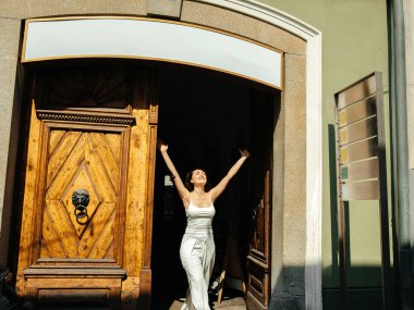 Neşeli kadın kırsal geçitte zarif beyaz elbisesiyle gün ışığını kutluyor.