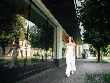 Kendine güvenen kadın şehir ortamında modern mimari ve yansıtıcı camla yürüyor.