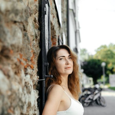Şehir merkezinde taş duvara yaslanan ve arka planda bisikletleri olan bir kadın.