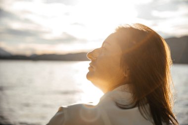 Kafkasyalı olgun kadın göl kenarında günbatımının tadını çıkarıyor.