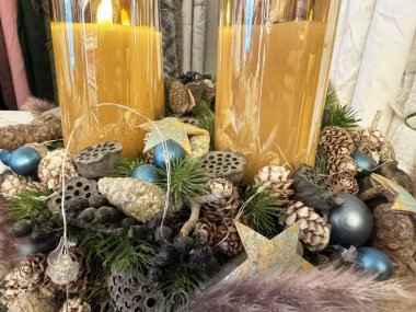 Elegant candle centerpiece with pinecones and blue ornaments for festive decor. clipart