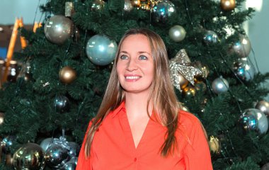 Beyaz kadın yetişkin süslenmiş Noel ağacının önünde gülümsüyor.