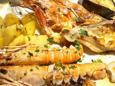 Karides, ıstakoz, balık ve otlarla süslenmiş patatesli ızgara deniz ürünleri tabağı..