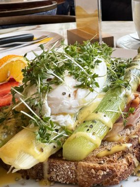 Tost üzerine haşlanmış yumurta, kuşkonmaz ve taze lahanayla süslenmiş Hollandez soslu gurme kahvaltısı..