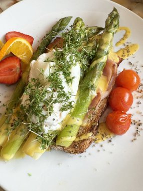 Haşlanmış yumurta, kuşkonmaz ve kızarmış ekmek üzerine taze meyve..