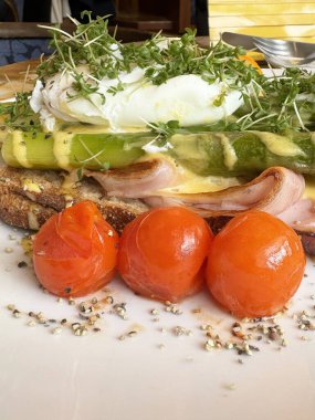 Gourmet sandwich with prosciutto, poached egg, asparagus, and cherry tomatoes on rustic bread. clipart