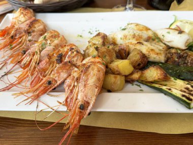 Izgara deniz ürünleri ve sebzeler ve yanında kızarmış patates..