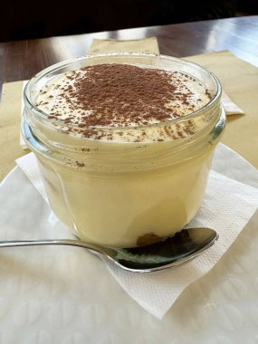 Cam kavanozda tiramisu tatlısı ve beyaz tabakta kaşık..