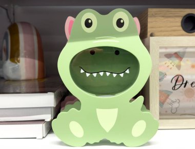 Green dinosaur-themed photo frame with cute cartoon design on shelf display. clipart