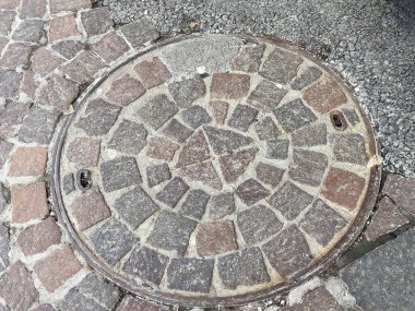 Round cobblestone manhole cover on textured pavement. clipart