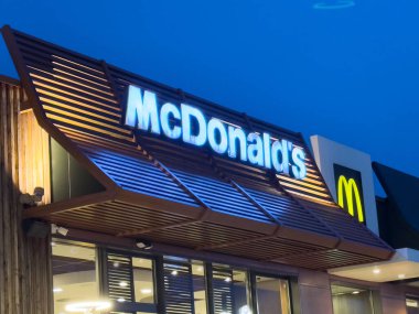 Modern McDonald 's restoranı geceleri aydınlık logo ve mavi gökyüzü arka planıyla.