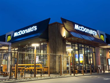 Modern McDonald 's restoranının dış mekanı geceleri aydınlatılmış logo ve oturma düzeniyle..