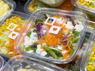 Plastik kabın içinde havuç, marul ve peynirle karışık taze salata ve mısır küveti..