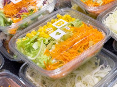 Şeffaf kabın içinde taze sebze salatası ve doğranmış havuç ve mısır..