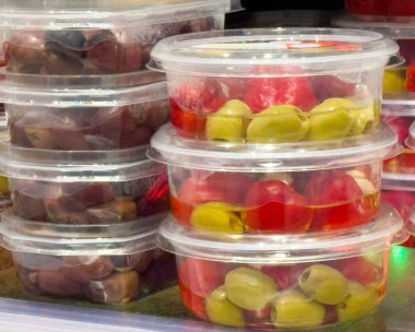 Raflarda sergilenen plastik kaplarda çeşitli zeytinler ve biberler.