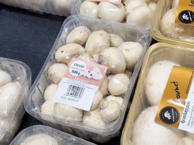 Süpermarkette paketlenmiş beyaz düğmeli mantarlar sergileniyor.