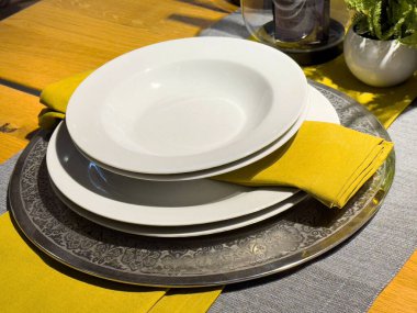 Beyaz tabaklar ve ahşap yüzeyde sarı peçeteler olan zarif bir masa..