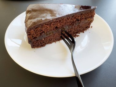 Beyaz tabakta çatallı, lezzetli bir dilim çikolatalı pasta..