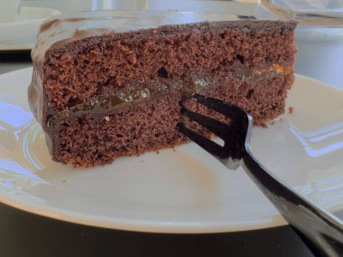 Lezzetli bir dilim çikolatalı pasta, beyaz tabakta zengin jöleli..