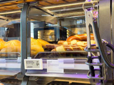 Pastane vitrininde fiyat etiketleri ve maşayla çeşitli ekmek ve krakerler..