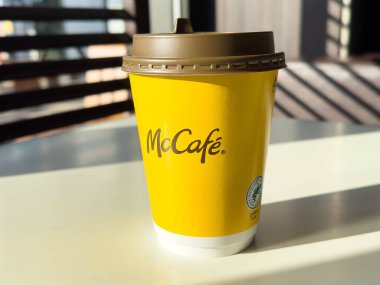 McCafe kahve fincanı güneş ışığı gölgeli bir masada, canlı sarı tasarım ve markalaşma sergileniyor, içecek pazarlama ve kahve kültürü konsepti için mükemmel.