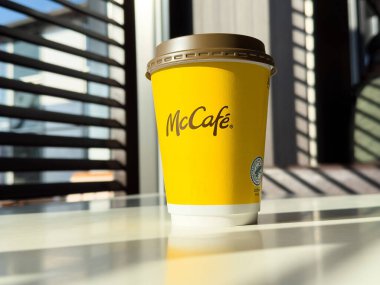 McCafe kahve fincanı, güneşli bir masada güneşlenerek sıcak bir atmosfer yaratıyor. Kahve severler ve kafe kültürü kavramı için mükemmel.