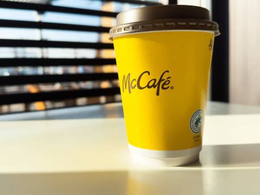 McCafe kahve fincanı parlak bir masada, güneş ışığı perdelerin arasından akıyor, canlı sarı tasarım ve davetkar atmosfer sergiliyor, kahve kültürü konsepti