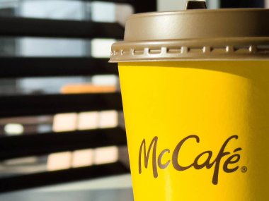 McCafe kahve fincanı parlak sarı renkli arka planda bulanık bir marka logosu sergiliyor, kahve kültürünü ve keyif kavramını temsil ediyor.