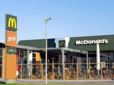 McDonald 's restoranının dış görünüşü modern mimari, canlı tabela ve açık hava oturma alanı, fast food yemek deneyimini temsil ediyor.