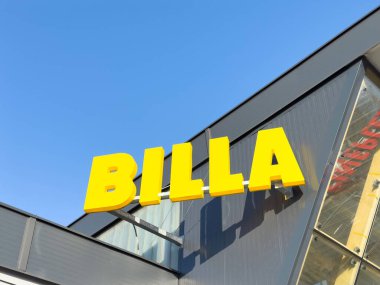 BILLA süpermarket işareti açık mavi gökyüzüne karşı modern mimari sergileniyor ve perakende satış ortamında canlı markalaşma sağlıklı alışveriş kavramı