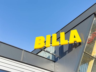 BILLA süpermarket işareti açık mavi gökyüzüne karşı modern mimari ve canlı markalaşma, perakende alışveriş kavramını temsil ediyor