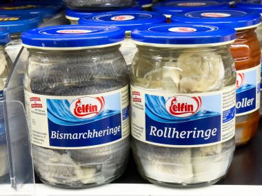 Süpermarketin rafında sergilenen turşulu ringa balığı kavanozları çeşitli balık ürünlerini sergiliyor, geleneksel mutfak lezzetlerini ve sağlıklı beslenme kavramını ön plana çıkarıyor