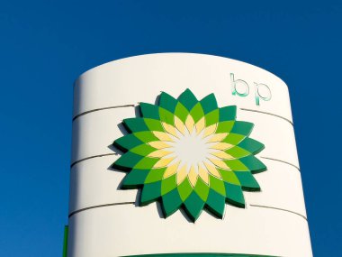BP logosu belirgin bir şekilde açık mavi gökyüzüne karşı, canlı yeşil ve sarı renkler sergiliyor, enerji ve sürdürülebilirlik kavramını temsil ediyor