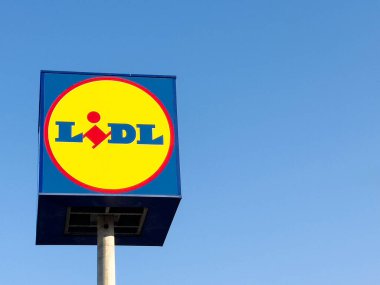 Lidl süpermarket tabelası açık mavi gökyüzü karşısında canlı renkler ve markalar sergiliyor, perakende alışveriş deneyimi ve kolaylık kavramını temsil ediyor