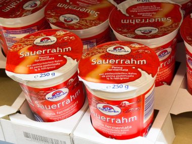 Kremalı ekşi krema konteynırları süpermarketin raflarında güzelce istiflenmiş canlı ambalajlar ve mutfak meraklıları ve sağlıklı beslenme konsepti için besleyici bilgiler sergiliyorlar.