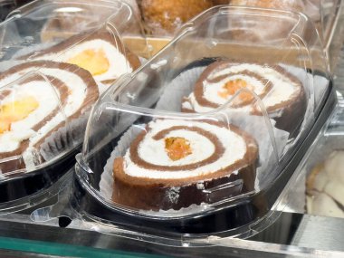 Bir pastanenin açık plastik kutusunda sergilenen kremalı nefis çikolatalı pasta. Çekici tatlılar ve tatlı ikramları sergiliyor.