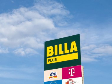 BILLA PLUS süpermarket tabelası açık mavi gökyüzüne karşı modern perakende satış deneyimi kavramını temsil eden marka logoları ve canlı renkler sergiliyor
