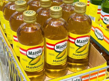 Bir mağazanın rafında sergilenen mısır yağı şişeleri Mazola markasının canlı ambalajını sergiliyor, pişirme yağı ürünlerindeki kaliteyi ve tazeliği vurguluyor, sağlıklı pişirme kavramını vurguluyor