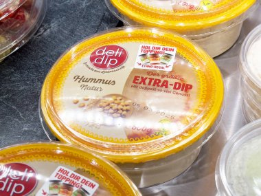 Ekstra sos etiketli canlı sarı bir kabın içine bandırılmış kremalı humus. Toplantılar ve sağlıklı beslenme konsepti için lezzetli bir atıştırma seçeneği sunuyor.