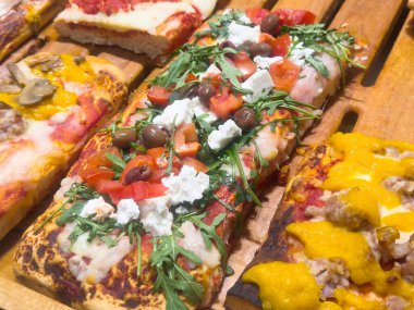 Peynir, zeytin, roka ve ahşap tahta üzerinde biberli çeşitli lezzetli dilimlenmiş pizzalar..