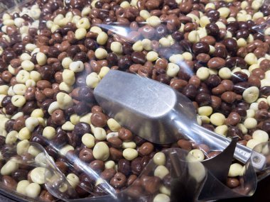 Açık bir kapta metal kepçeyle çikolata kaplı fındıklar..