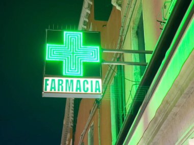 Parlak yeşil eczane işareti ve gece binanın dış tarafında kurşun haç var..