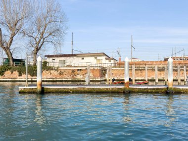 Güneşli bir günde rıhtım ve teknelerle sessiz bir kanal sahnesi.