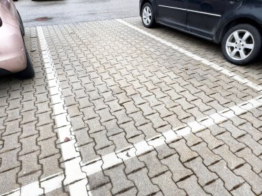 Tuğla döşeli arsada iki araba arasında boş park yeri.