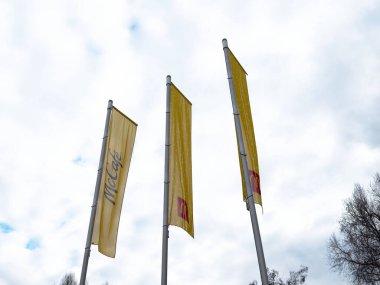 Bulutlu gökyüzüne karşı uzun direklerde üç sarı Mccafe bayrağı.