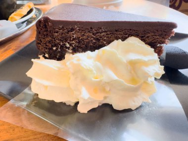 Kafe ortamında siyah tabakta kremalı zengin çikolatalı pasta dilimi..