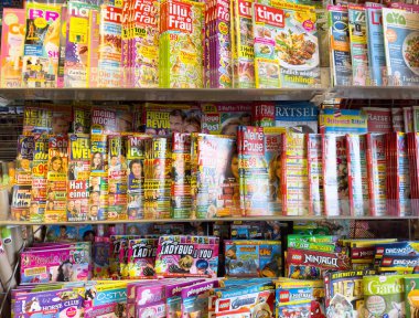 Alman dergisi ve bulmaca rafı bir gazete bayisinde çeşitli renkli kapaklar sergiliyor..