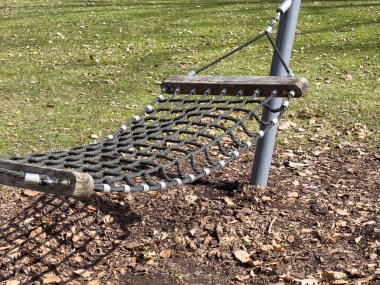 Yaprak kaplı park ortamında metal çerçeveli açık hava halat hamağı..